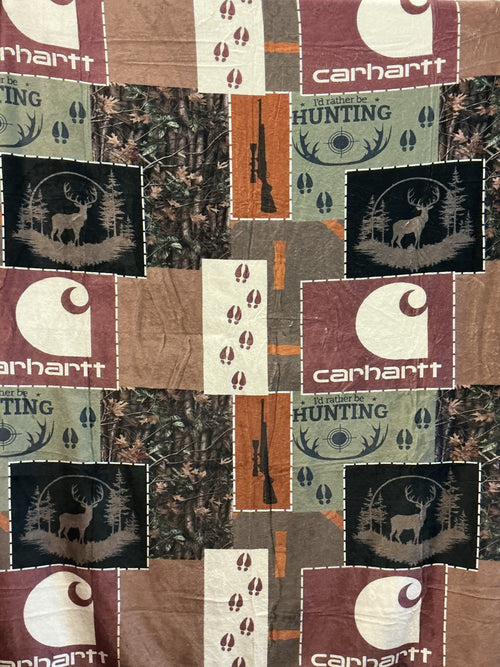 A Carhartt patchwork print 50 x 60” plush blanket. The blanket  features a mix of Realtree camouflage, brown and burgundy Carhartt logos, hunting silhouettes, and vertical orange-brown stripes.