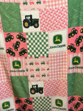 A patchwork pattern featuring John Deere themed fabric squares with green tractors, pink gingham, green checkered patterns, and solid green panels.