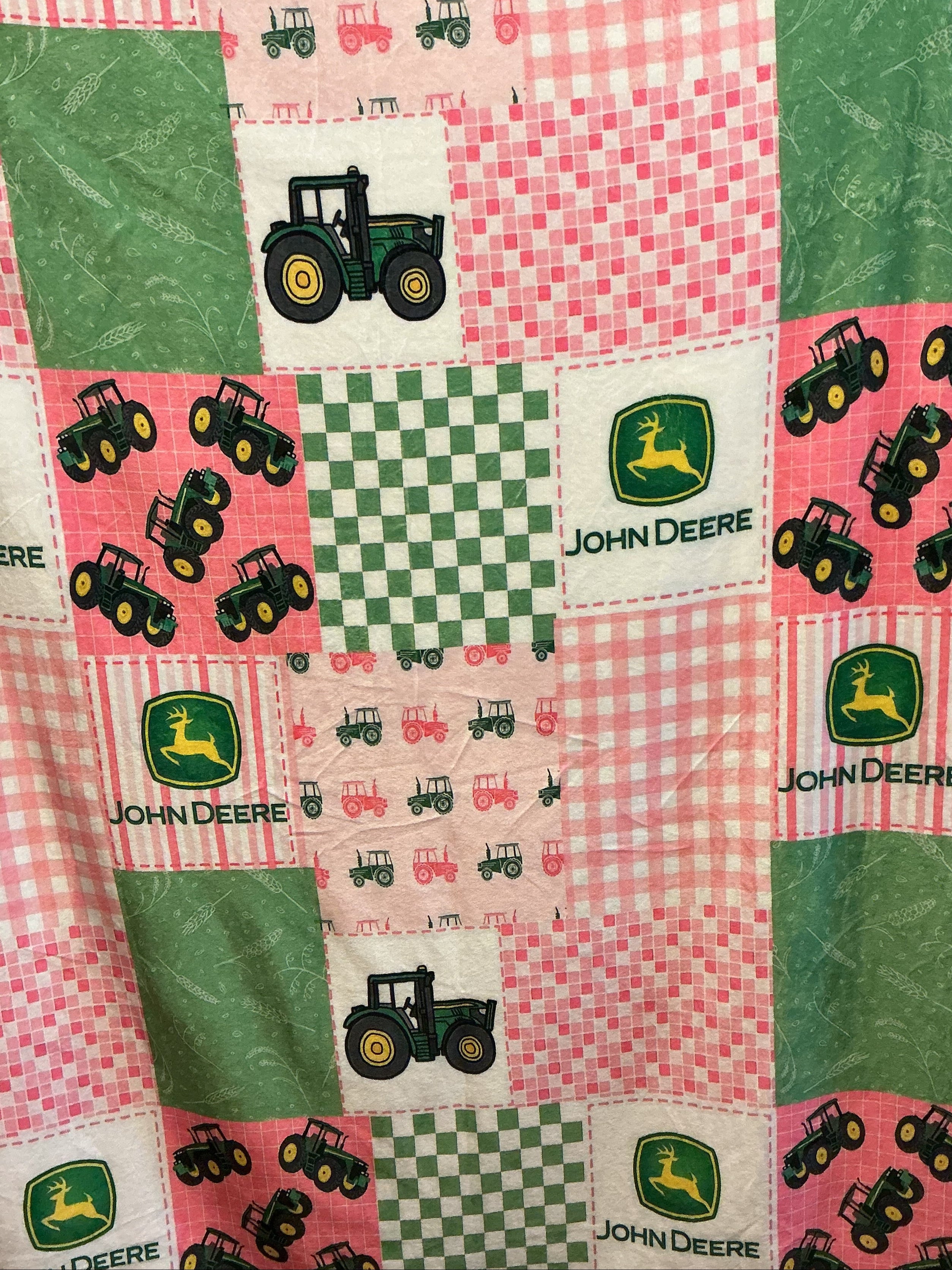 A patchwork pattern featuring John Deere themed fabric squares with green tractors, pink gingham, green checkered patterns, and solid green panels.