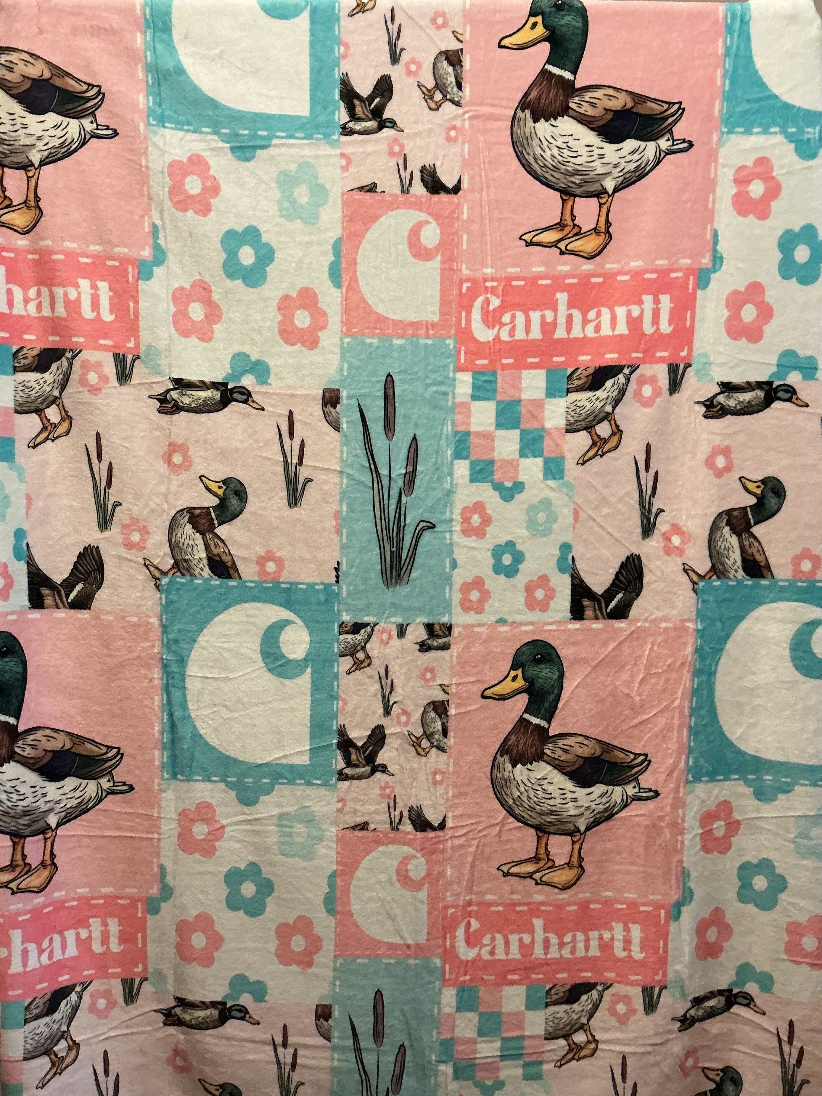 A patchwork print featuring a duck-themed design with illustrations of mallards, floral motifs, and the word 'Carhartt' printed on pink and teal sections.