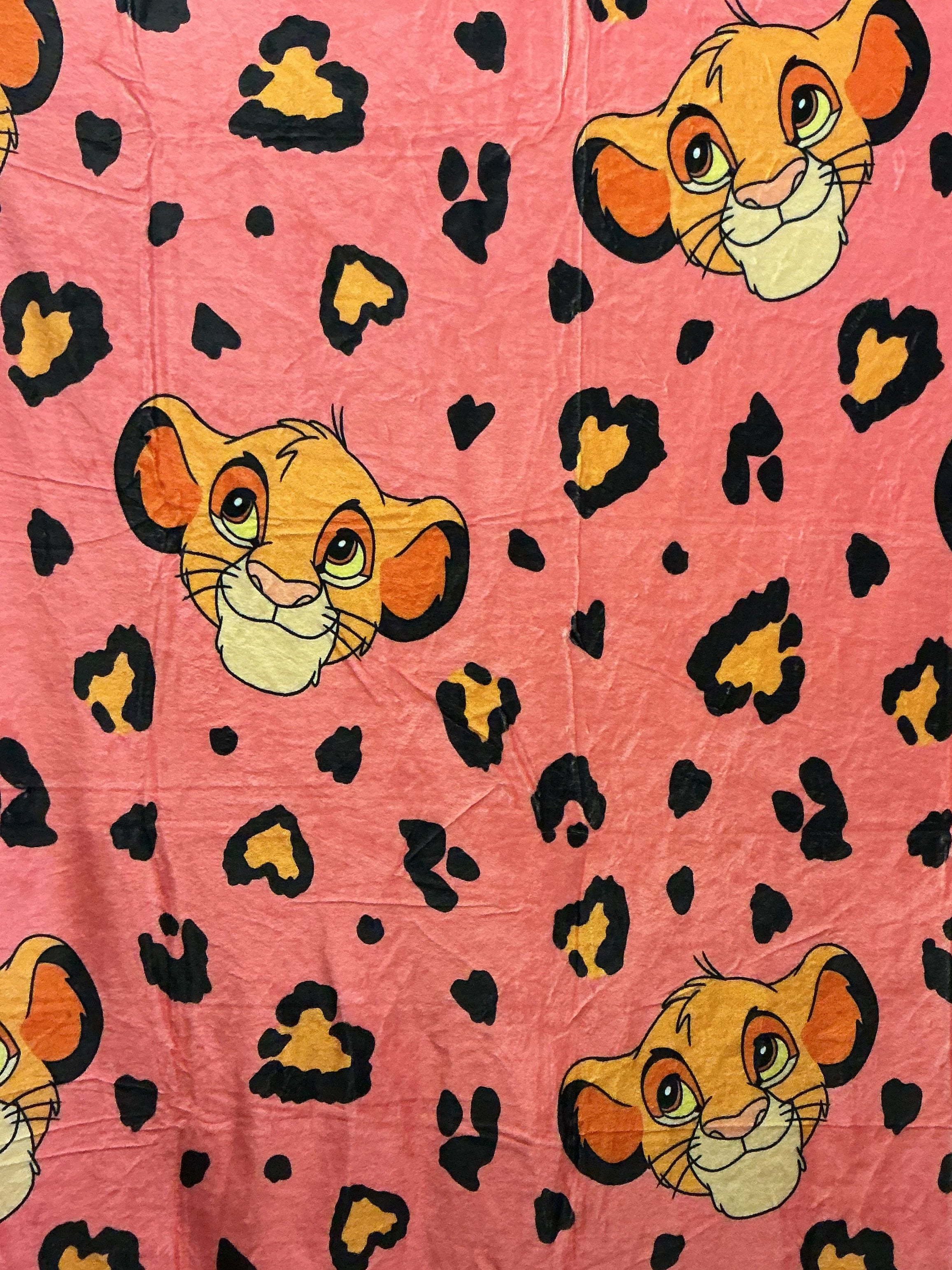 Pink fabric with an allover print of Simba's cartoon faces and black leopard spots.