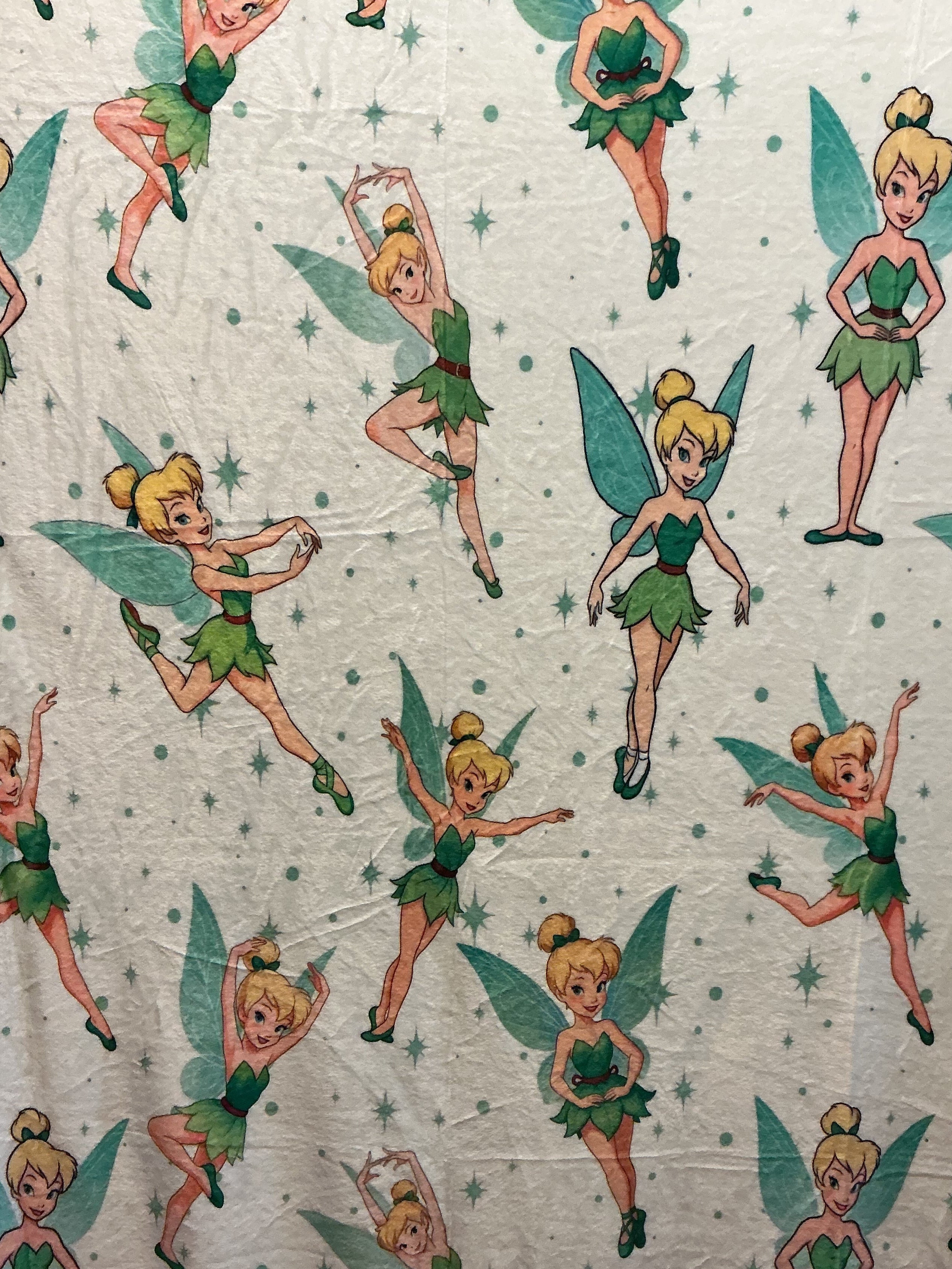 Plush blanket featuring Disney's Tinker Bell characters in green and yellow, set against a light cream background with small green stars.
